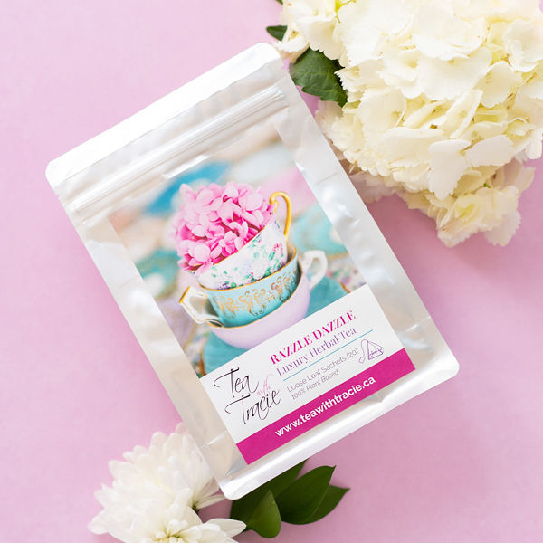 Razzle Dazzle raspberry lemonade herbal tea pouch by Tea with Tracie on a pink background with white flowers