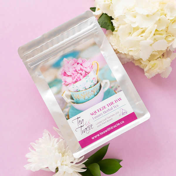 Squeeze the Day lemon ginger herbal tea pouch by Tea with Tracie on a pink background with white flowers